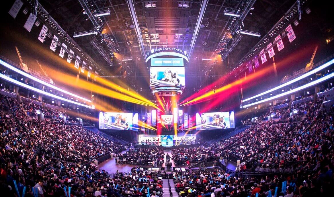 Een volgepakte arena tijdens een esports-evenement, waar fans het spel volgen op enorme schermen, omgeven door kleurrijke lichteffecten.